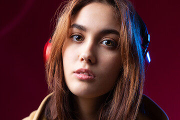 Young beautiful fashionable hipster girl dressed in a hoodie  listening to music in red headphones in a studio red dramatic background