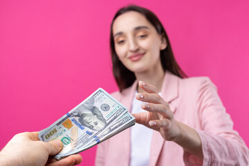 A woman in a pink jacket receives a bribe in dollars against a red background.