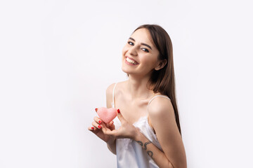 Beautiful smiling woman with clean skin, natural make-up and white teeth on a gray background. Holding a pink hygienic heart.