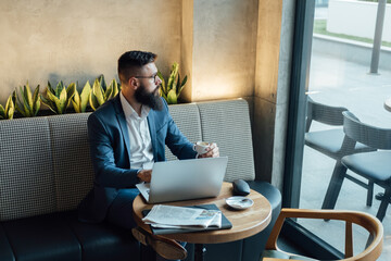 Serious Businessman Drinking Espresso and Working on Laptop Computer in a Cafe