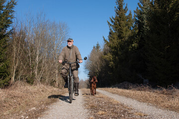 Spring has arrived and a hunter rides his bike through the forest accompanied by his Irish Setter...