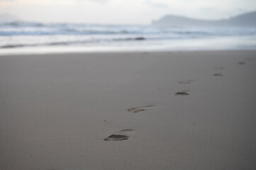 Footsteps on sandy beach and stormy sea waves at winter