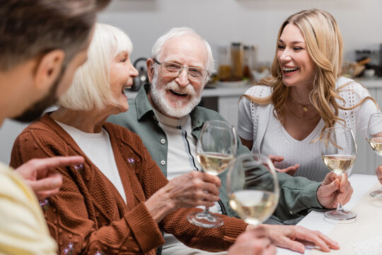 blurred man pointing with finger near cheerful family with wine glasses.