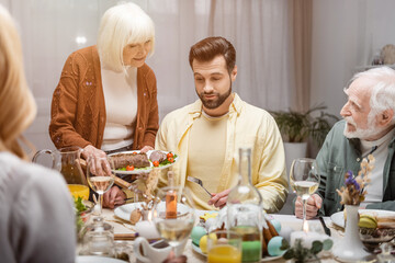 senior woman holding fried meat near adult son during easter family dinner.