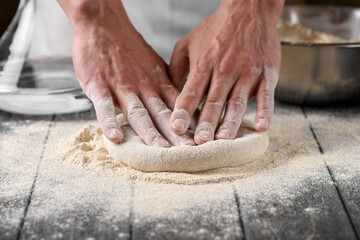 The process of preparing dough in the kitchen. The cook kneads the dough from wheat flour. Cook's hands. Water and flour on a wooden table.
Bakery or pizza baking.
Close-up shot, selective focus.