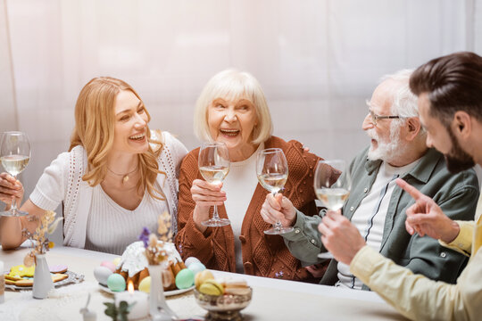 man pointing with finger near happy family holding wine glasses during festive dinner.