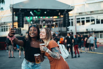 Two beautiful friends taking selfie with a smartphone on a music festival