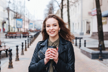 young curly woman wearing black leather jacket walking, drinking coffee outdoor