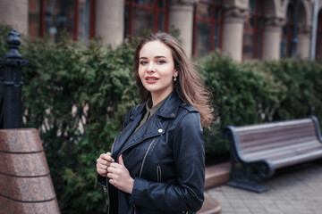 Young woman in black leather jacket walking on city street