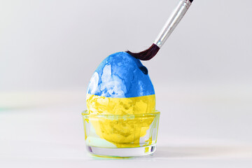 Brush is painting an Easter egg in blue and yellow,  colors of the Ukraine flag, symbol of...