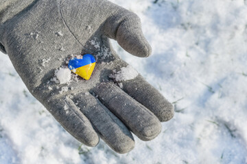Yellow and blue small heart in a hand with glove, colors of the Ukraine flag, symbol of preserving the country from the crisis of the Russian invasion, copy space