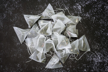 A pile of pyramid tea bags filled with green and black fruit-flavored teas lie on a dark,...