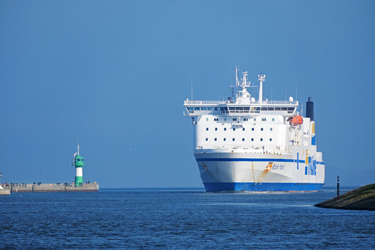 Lubeck, Germany, March 3, 2022: Large ferry boat between the lighthouse and the Priwall shore entering the port of Lubeck Travemunde on the Baltic sea, blue sky with copy space