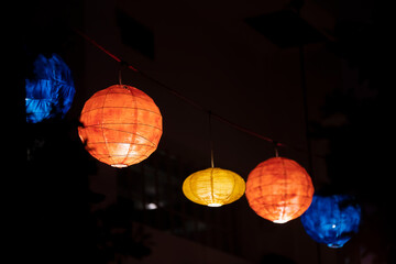 Colorful lampions and lanterns on wire shine at night in the garden. A wedding, event or festival...