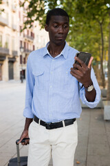 African american tourist on the street writes message on the mobile phone screen