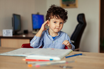 Preschool education online. A cheerful and energetic preschooler at the computer is engaged, next to notebooks, pencils. Lesson with a teacher remotely.
