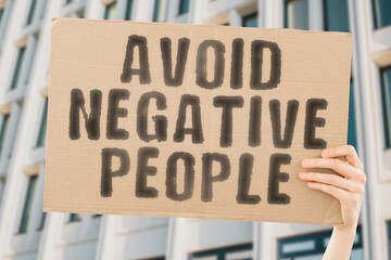 The phrase " Avoid negative people " on a banner in men's hand with blurred background. Access. Rude. Hurt. Upset. Worry. Toxic. Panic. Choice. Disgust. Strong. Protect. Feeling. Frustration