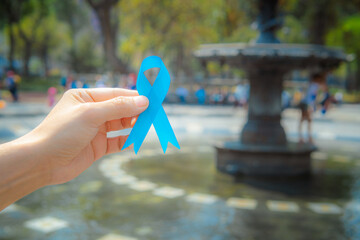 A hand holds a blue ribbon in support of people with prostate cancer.