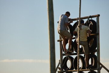 Train like theres no finish line. Shot of men climbing over an obstacle at bootcamp.