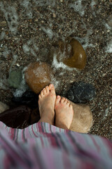 women's feet relax on the sand in sea water. A woman in a striped pink dress, a trip and a lifestyle on the coast of the sea