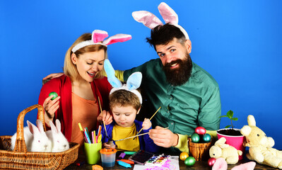 Happy family painting Easter eggs. Mother, father and son in bunny ears on holidays.