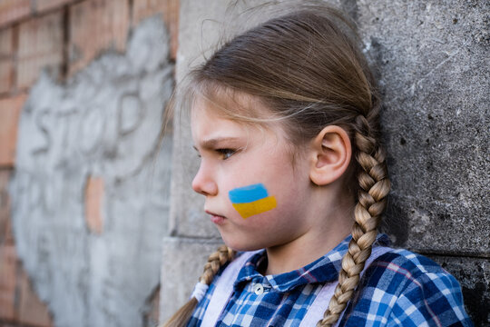 Portrait of a frightened child girl with painted flag on the cheek in yellow-blue colors of the Ukrainian flag. Peace and protection children concept