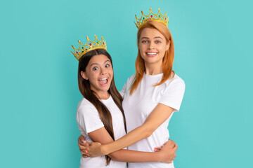 Happy woman and girl child in crowns hug smiling blue background, mother - obrazy, fototapety, plakaty