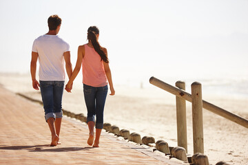 Enjoying a walk down memory lane. Rear view shot of a young couple walking along the beach holding hands.