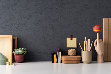Office desk with notebooks, desk objects, office supplies, books, folder and plant on a dark grey background..