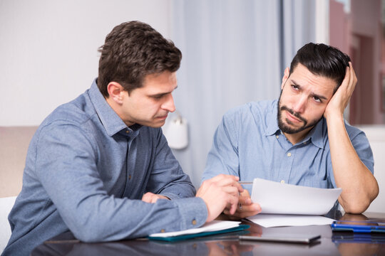 Two upset male friends looking worriedly at papers at home table