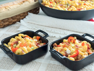 Two individual servings of baked macaroni and cheese with the skillet and loaf of bread in the background