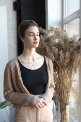 Fototapeta premium young beautiful woman pose near the window in the studio, standing in a sweater, standing in a black T-shirt