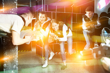 Emotional girl with laser pistol playing laser tag with friends on lasertag gaming arena