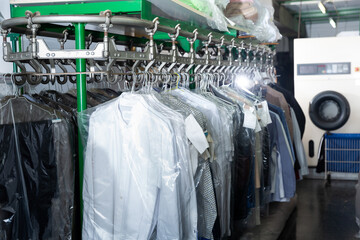 Clean clothes packed in plastic bags hanging on racks after cleaning at dry-cleaning facility