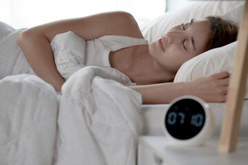 Young woman continues to sleep after turning off alarm clock in morning.