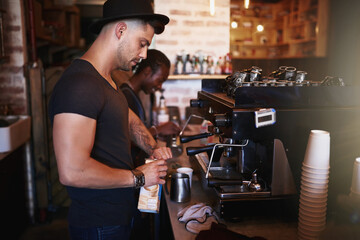Coffee savviness. Shot of a young man operating a coffee machine in a cafe.