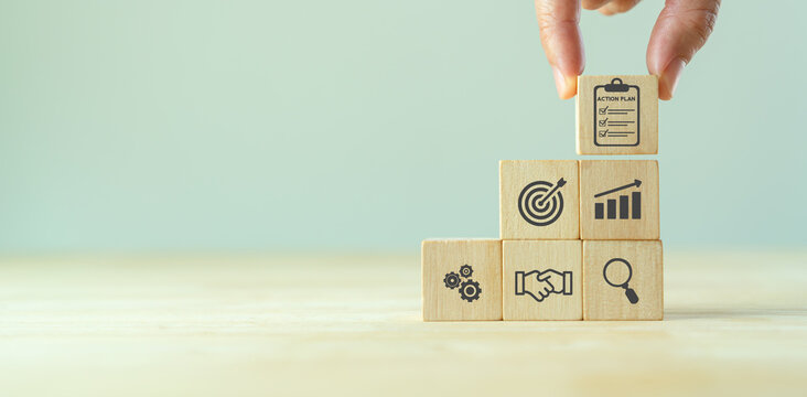 Action plan, business strategy and direction concept. Business resolution and development. Hand hold stacking wooden cube with action plan icon standing with goal, plan, action icon on grey background