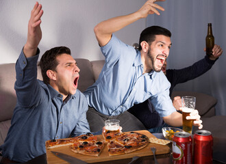 Group of male friends watching football match on tv at home and having fun together