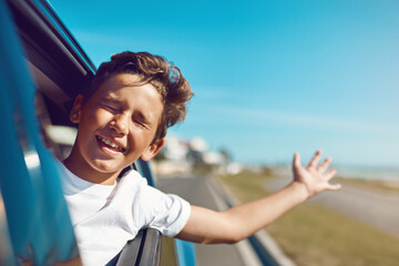 Feel the wind in your hair - and your face. Shot of a happy young boy leaning out of the car window on a trip to the beach.