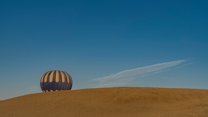 A bright yellow-blue balloon rises above a sand dune. The background is a clear azure sky. Copy space. Egypt. Luxor