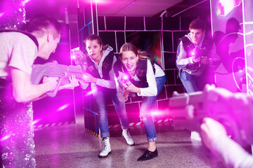 Emotional girl with laser pistol playing laser tag with friends on dark labyrinth