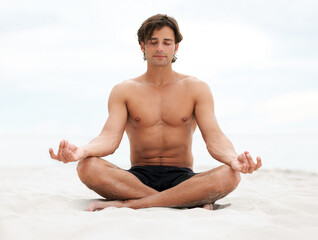 Be still and listen to what nature has to say. Young handsome man sitting on the beach meditating.