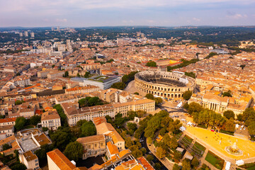 Fototapeta na wymiar Drone view of ancient Roman amphitheatre Arena of Nimes on background of reddish tiled roofs of residential buildings on summer day, France