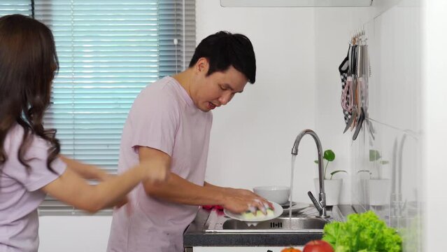 stressed young couple conflict in their kitchen, angry woman pointing hand to man for washing dishes