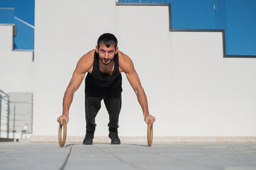 A man in black sportswear doing ring push-ups outdoors.