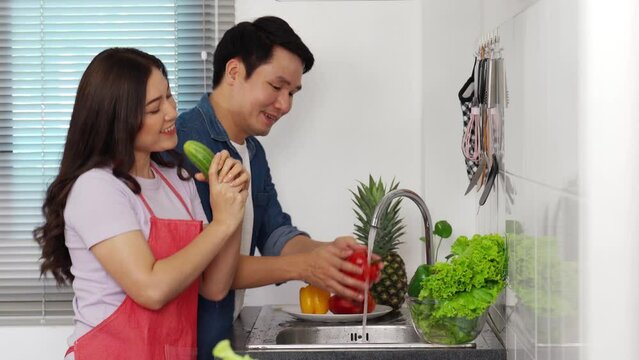 cheerful young couple dancing while washing vegetables in the sink in the kitchen at home. (cooking together)