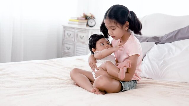 4K, 50 fps aborable gril Asian, carries her baby brother and sits on the bed in her bedroom, happily and happily. happy family concept
