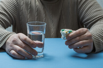 The man is holding a glass of water and pills.