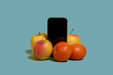 Online shopping. A smartphone with a black screen, mandarines and apples