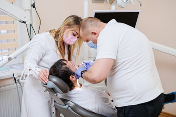 The dentist doctor looks at the patient's teeth and holds dental instruments near the mouth. The assistant helps the doctor. They wear white uniforms with masks and gloves. Dentist. Dental office